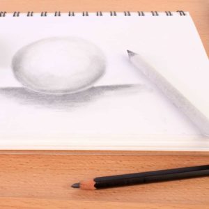 Drawing and shading of a sphere in a spiral note with blending stump and pencil on a table.