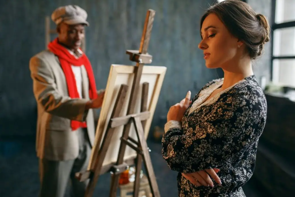 An Artist standing in front of easel and drawing a women depicting drawing from life