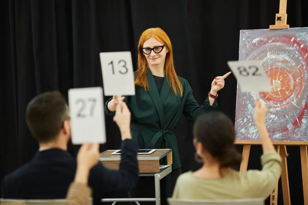 Picture of a lady auctioning art explaining economic benefits of art