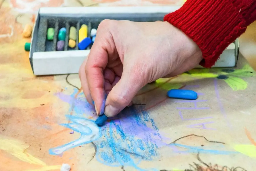 An artist hand drawing a bird using pastel