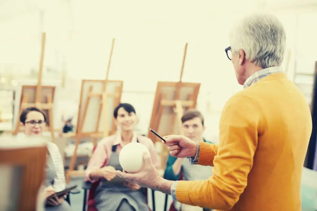 an art teacher explaining the shape and shades of a sphere holding in his hand to three students