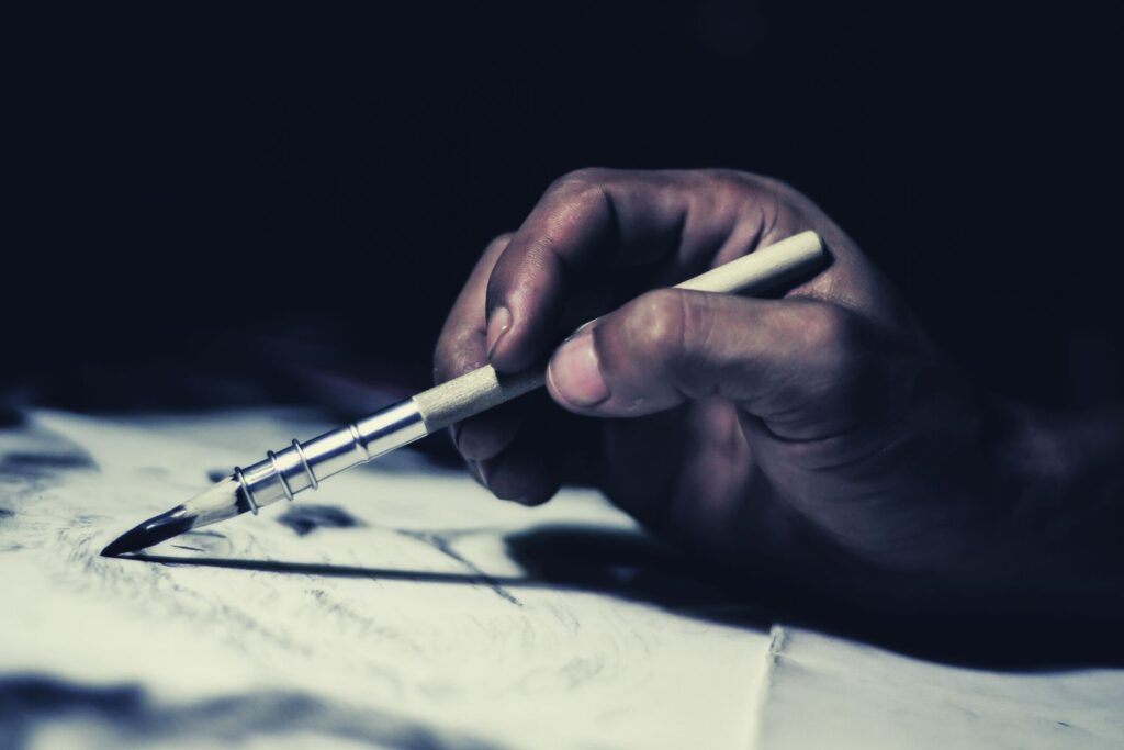 A hand drawing a sketch using a charcoal on a paper. The hand is holding a pencil holder.