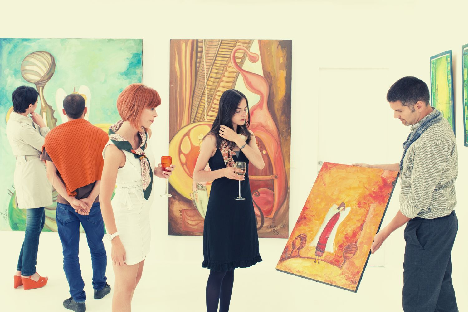 Two ladies are checking a painting and a man is explaining a painting in an art gallery
