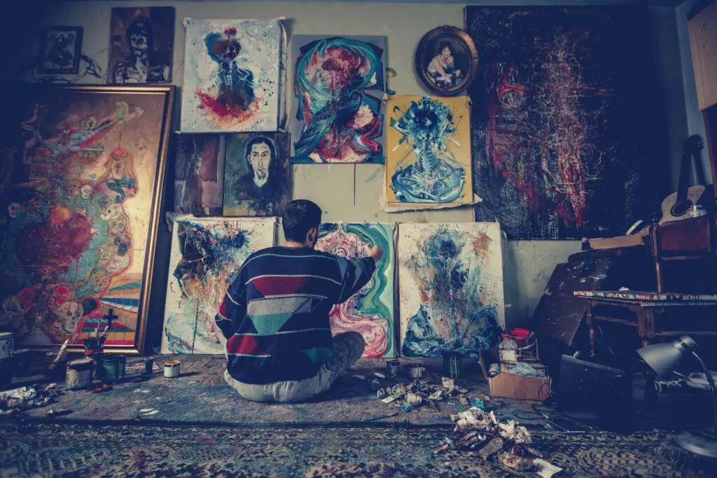 a budding artist sitting on the floor and painting and there are several paintings on the wall.